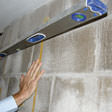 Man using level on cinder block basement wall to diagnose a bowing wall